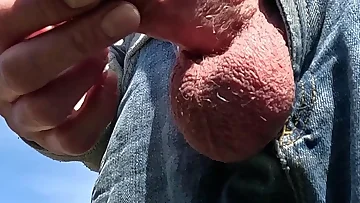 This British bloke strips down to just his jeans for some outdoor wanking action. He jerks his uncut cock until he unleashes a massive cumshot all over himself.