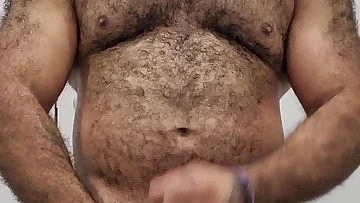 A hairy muscular bear strokes his cock with a penis ring after an intense workout session. This rugged amateur shows off his beefy body and thick dick while getting off.